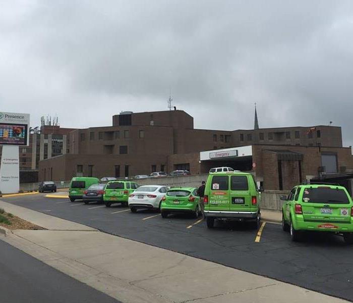 Five SERVPRO cars and two regular cars outside of a brown hospital building