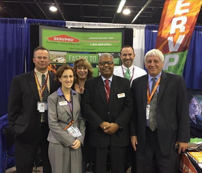 six men and women standing in a SERVPRO booth