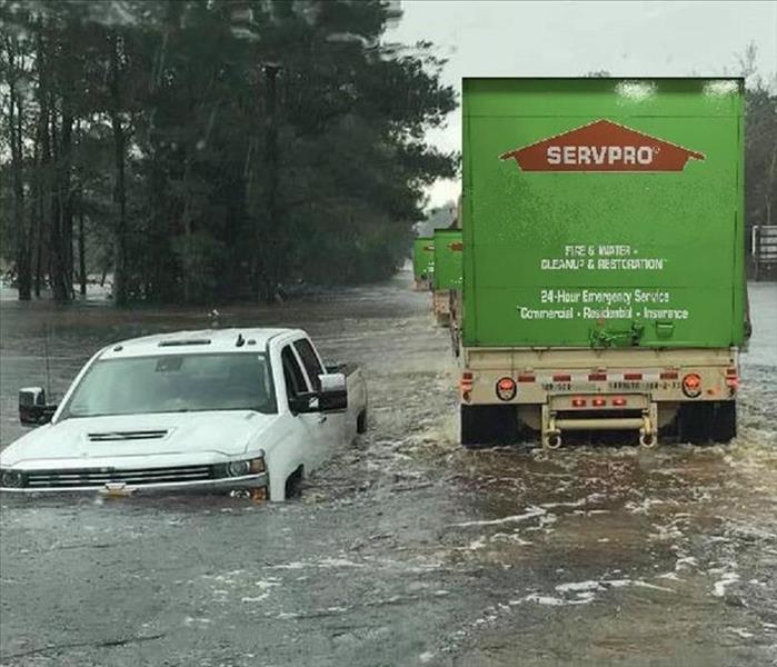 White truck sunk in water next to a line of SERVPRO trucks