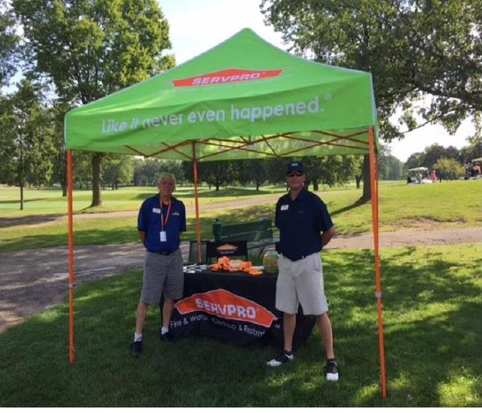 Two male SERVPRO representatives standing near a SERVPRO table with green and orange merchandise.