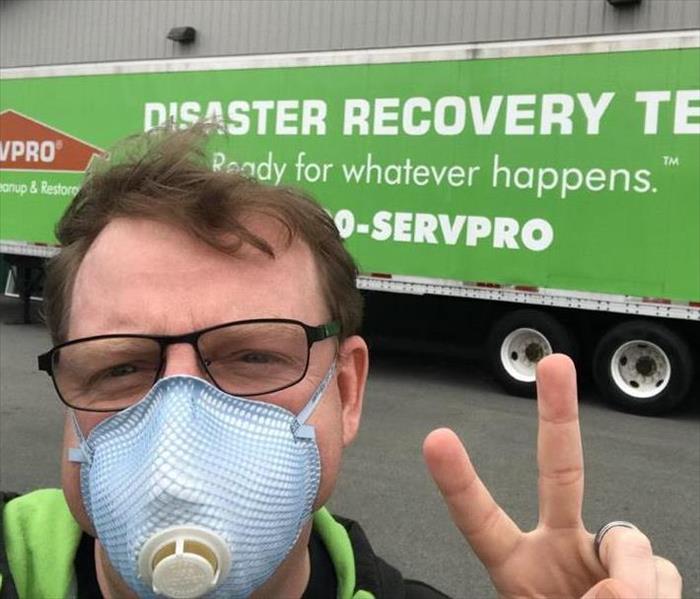 man with a mask standing in front of a SERVPRO green truck